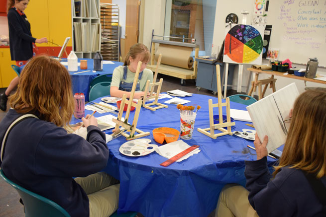 Teens gathered at table with blue table cover, painting