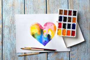 Watercolor heart on paper surrounded by color pallets and brush set