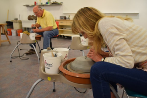 Two artists leaning over pottery turn tables