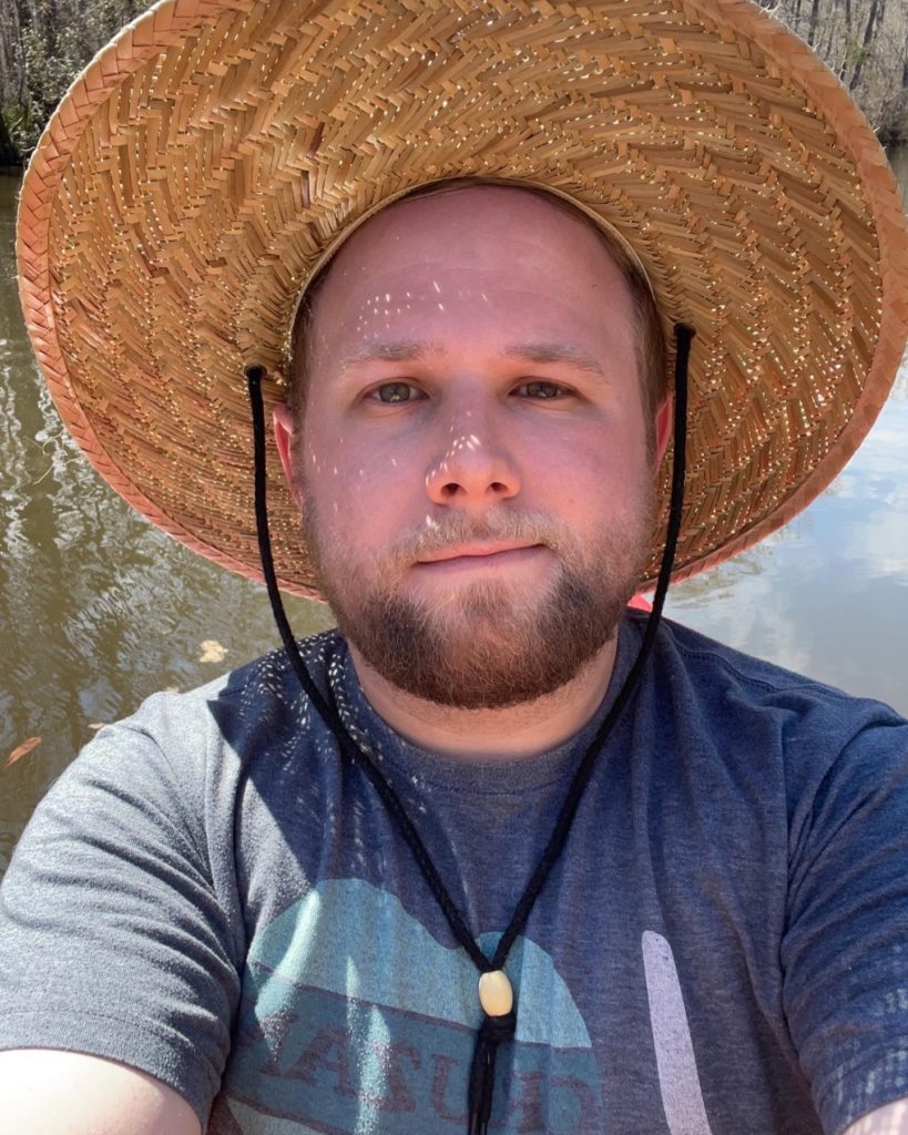 Selfie of Ben Kaiser in a sun hat on the water